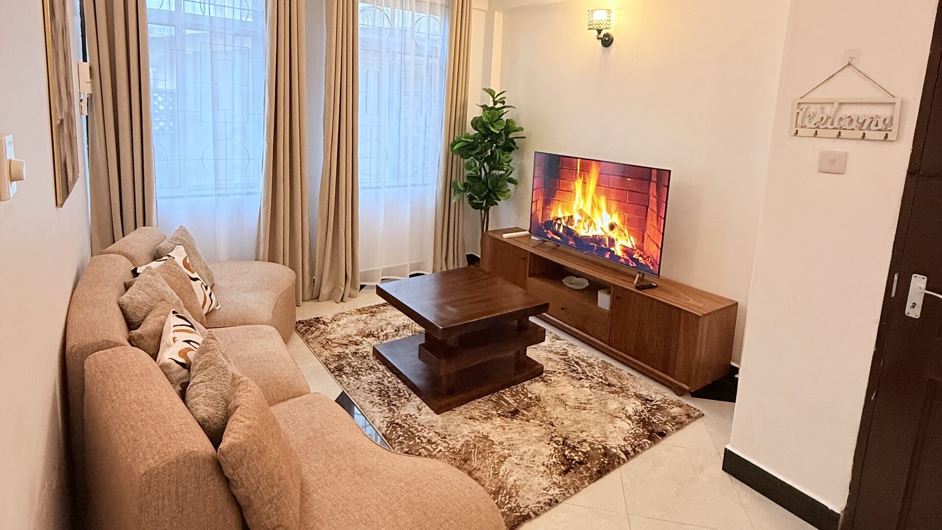 Warm living room of the Mikocheni apartment with curved sofa, rug, and smart TV